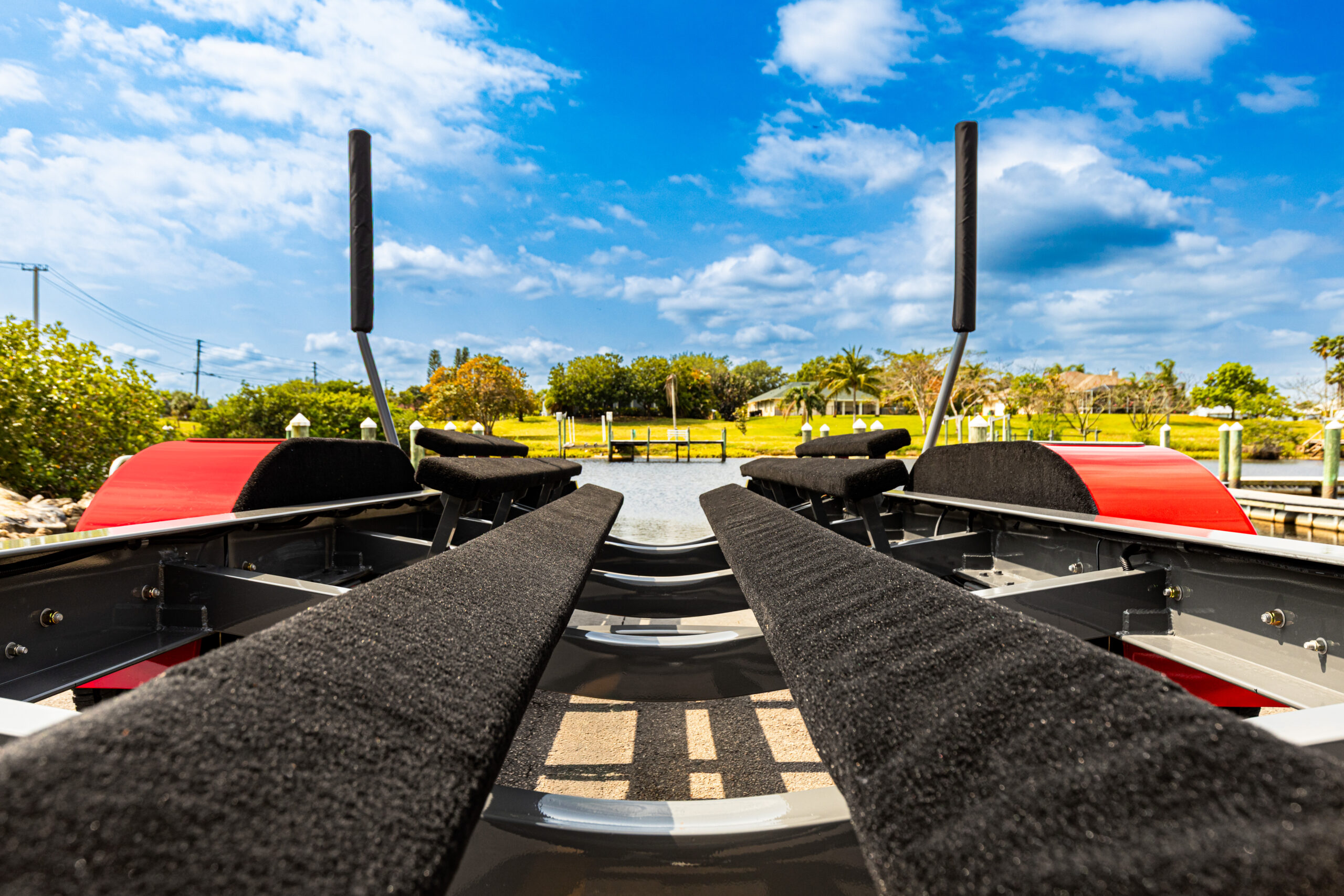 EZL-1-18 EZ Loader trailer bunks with padded black carpet, red fenders, and boat guides, ready for launch under a bright blue sky