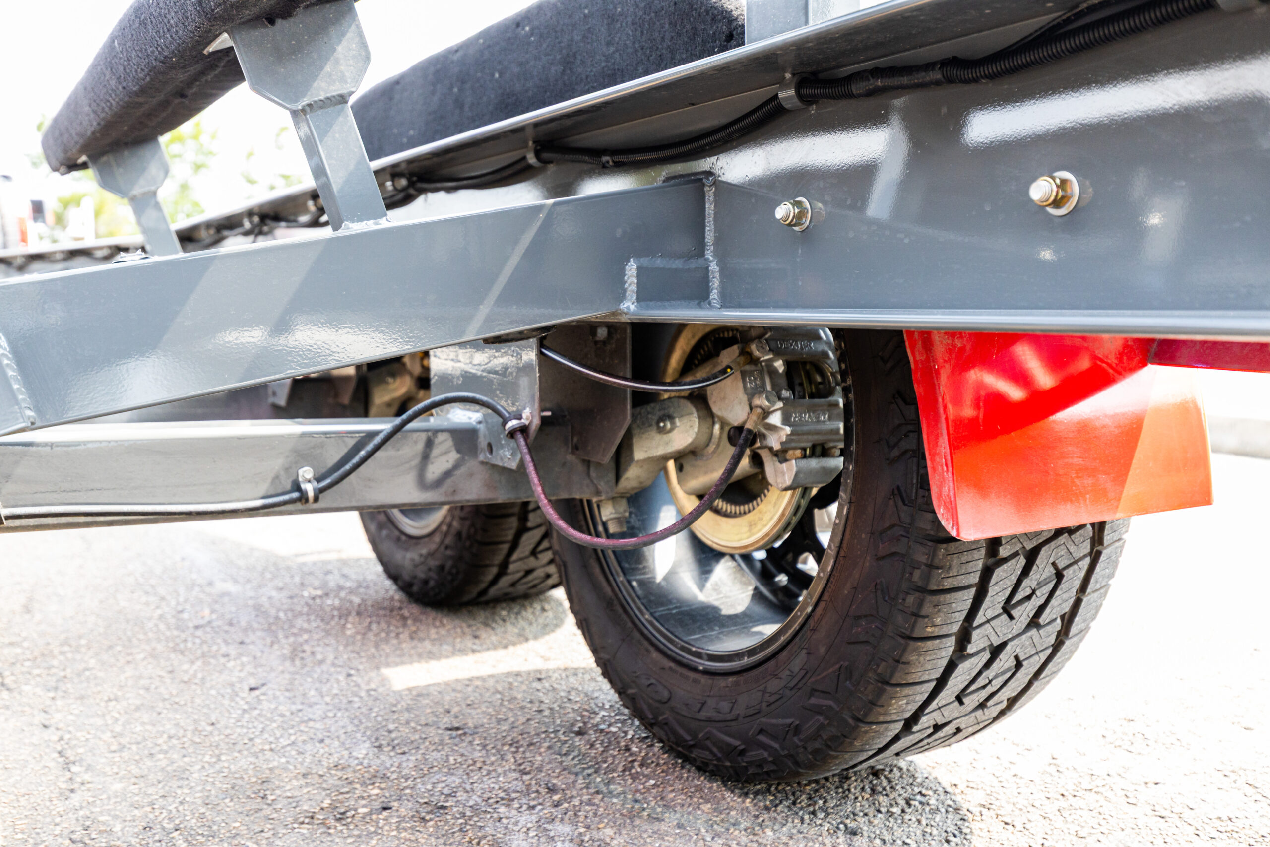EZL-1-25 Close-up of a boat trailer's axle and brake system, showcasing disc brakes, wiring, and powder-coated steel frame near the wheels and red fenders