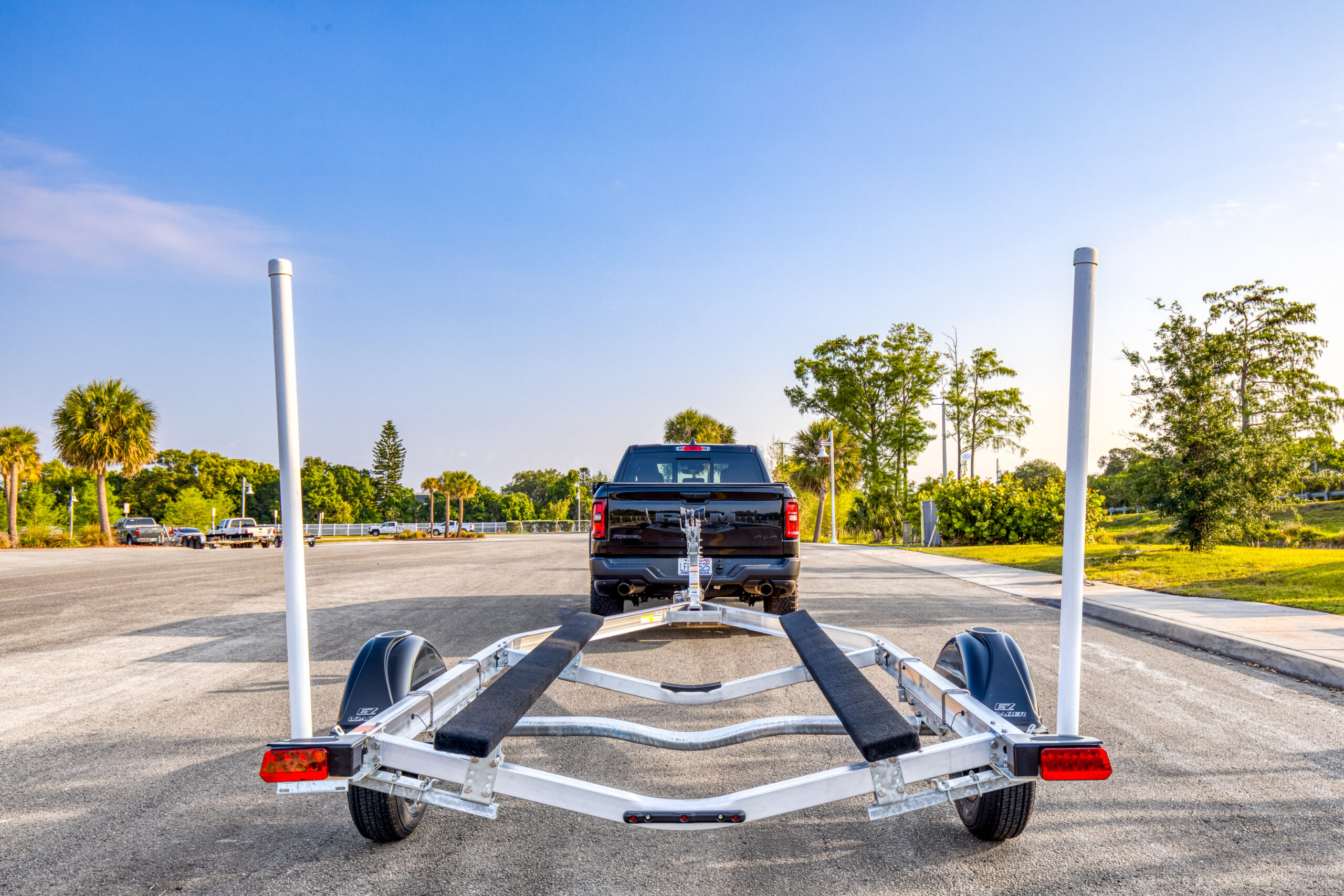 EZ Loader single axle aluminum boat trailer with carpeted bunks and guide posts hitched to black pickup truck on boat ramp lot